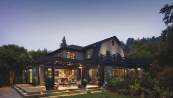 A view of of a house with lots of interior and exterior lighting, dark framing and a dusk backdrop.