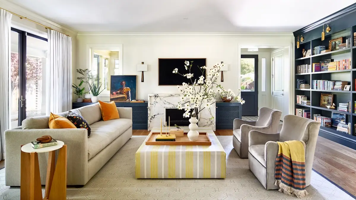 A cozy yet sophisticated living room with a marble fireplace, built-in navy bookshelves filled with books, and comfortable seating in warm neutral tones.