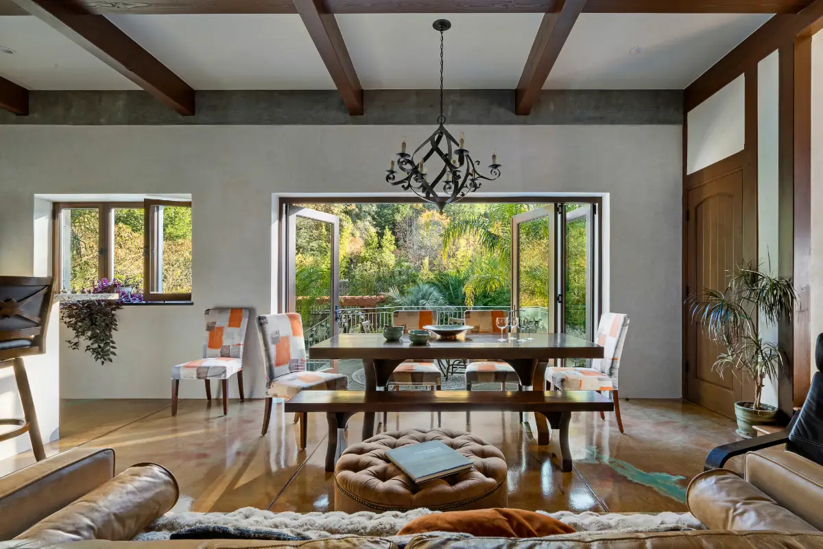 The ADU’s dining room with a large wooden table and colorful chairs, opening to a lush backyard garden through wide bi-fold doors.