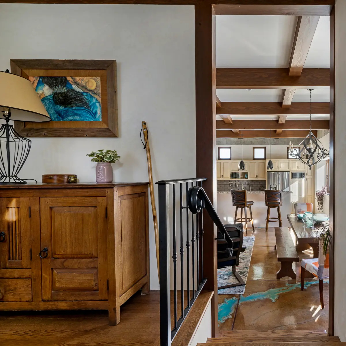A view from the stair landing into the ADU’s open living area, featuring a rustic wooden cabinet, framed artwork, and iron stair railings.