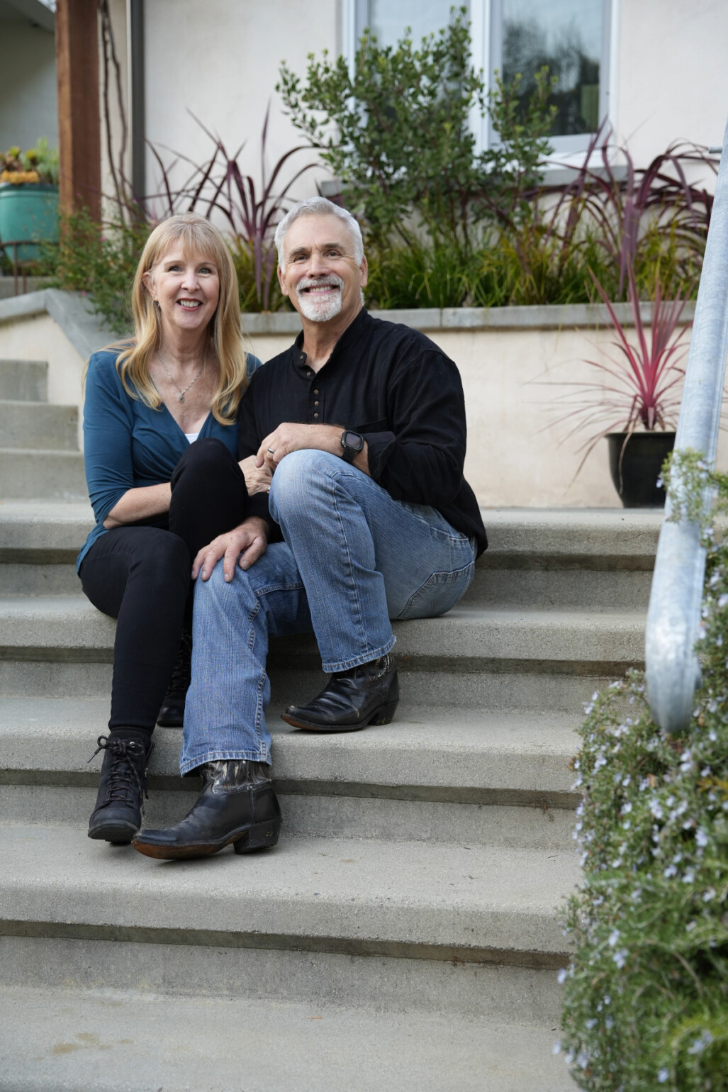 Nick and Sylvia Calder sitting together on the front steps of their concrete ADU in Fairfax, smiling warmly at the camera.