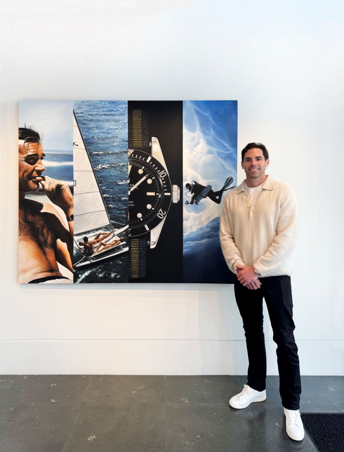Ryan Jones stands next to a painting of Sean Connery as James Bond, featuring a Rolex watch, a yacht, and a diver.