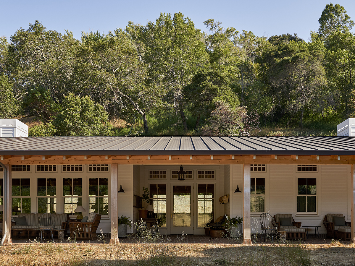 A creamy off-white shade house showcasing a covered porch and patio, blending harmoniously with its natural surroundings.