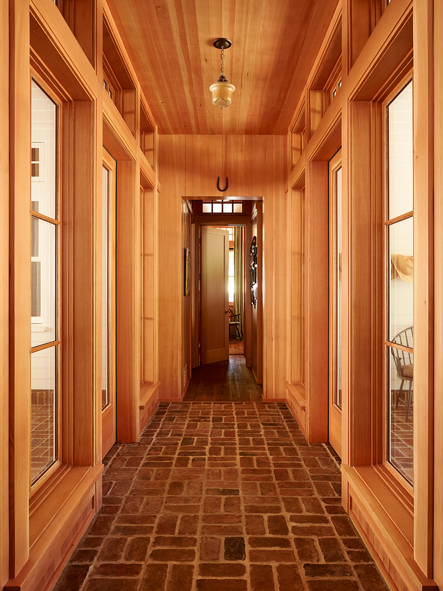 A window-flanked hallway featuring a brick floor creating a warm and rustic atmosphere.