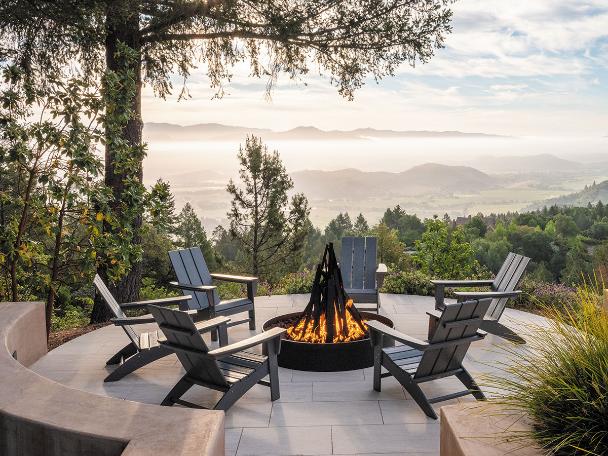 A cozy fire pit surrounded by chairs on a patio, with trees providing a natural backdrop.