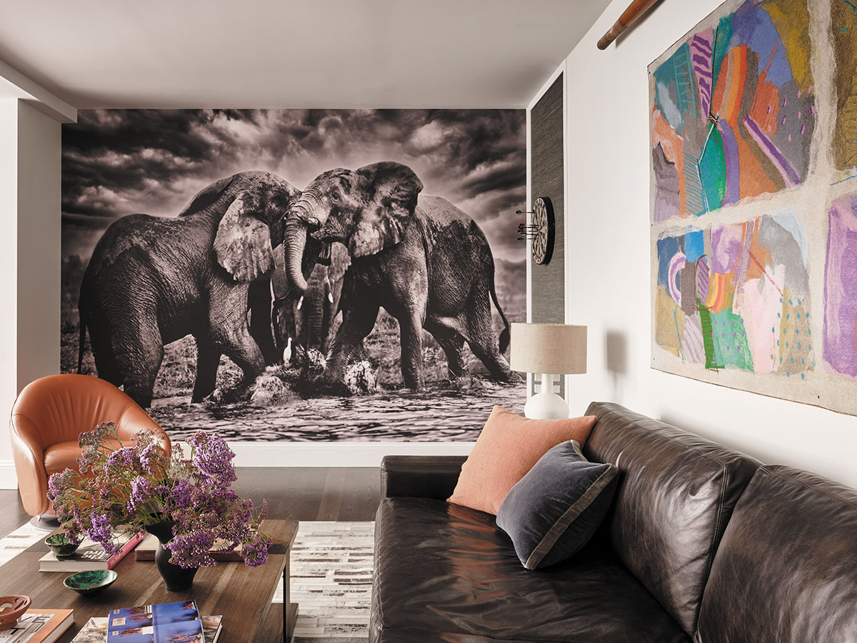 A cozy living room featuring a couch, coffee table, and a painting of elephants on the wall.