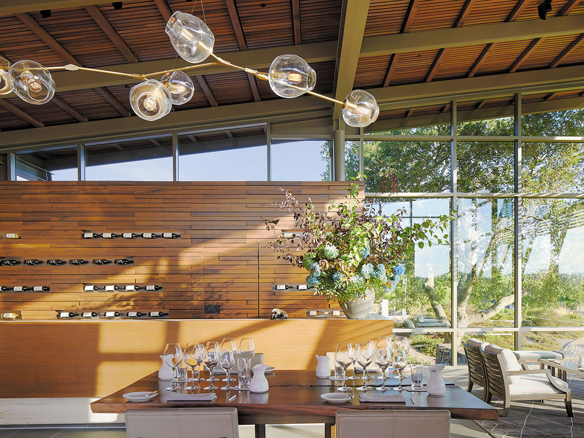 A restaurant interior featuring a table and chairs beside a large glass wall, allowing natural light to enter.