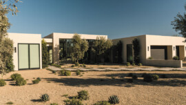 A contemporary house with a large driveway and greenery from nearby trees.
