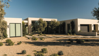 A contemporary house with a large driveway and greenery from nearby trees.