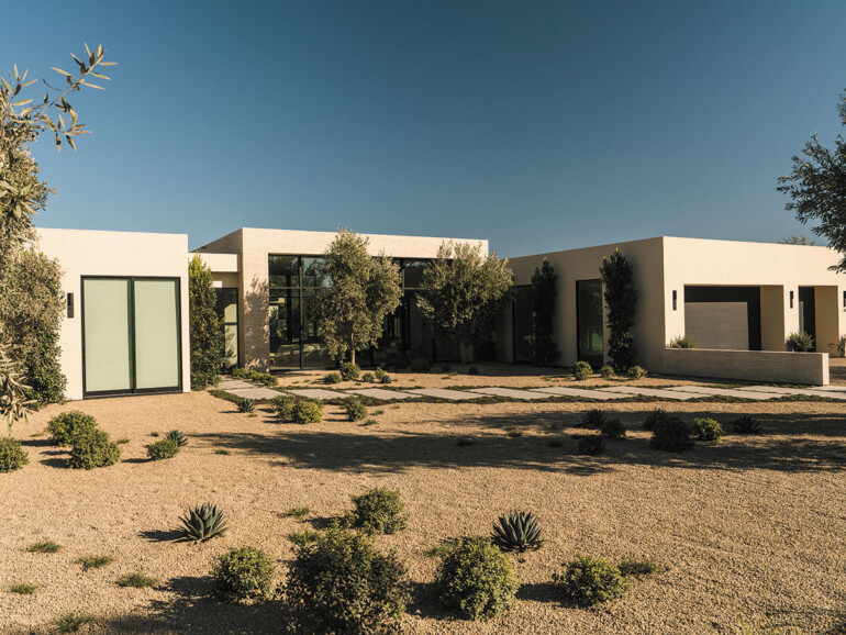 A contemporary house with a large driveway and greenery from nearby trees.