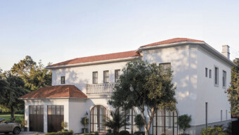 A white house with a red roof and a car parked in front on a sunny day.
