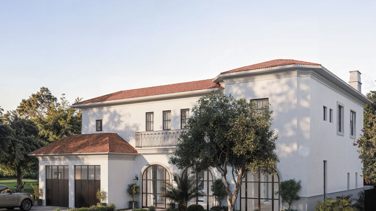 A white house with a red roof and a car parked in front on a sunny day.