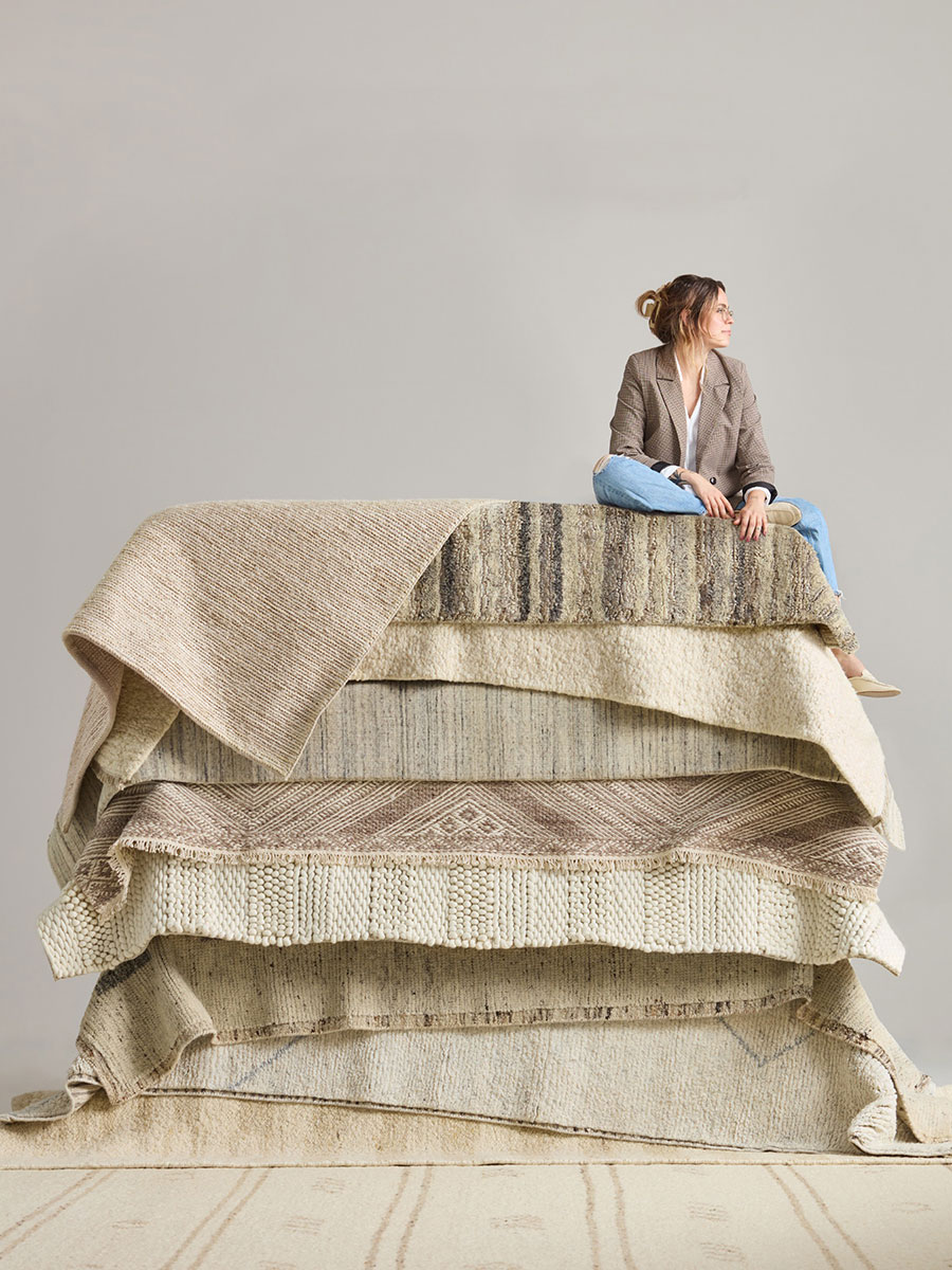 A woman sitting atop a colorful pile of rugs, smiling and enjoying her cozy surroundings.