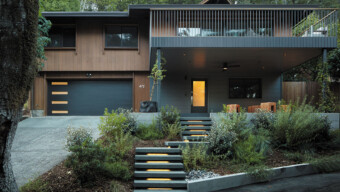 A house stands in front of a large tree, showcasing a harmonious blend of architecture and nature.