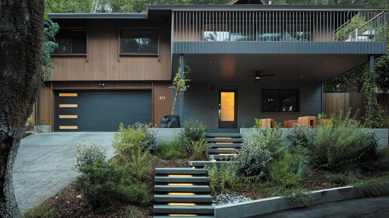 A house stands in front of a large tree, showcasing a harmonious blend of architecture and nature.