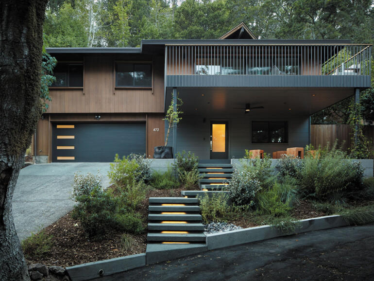 A house stands in front of a large tree, showcasing a harmonious blend of architecture and nature.