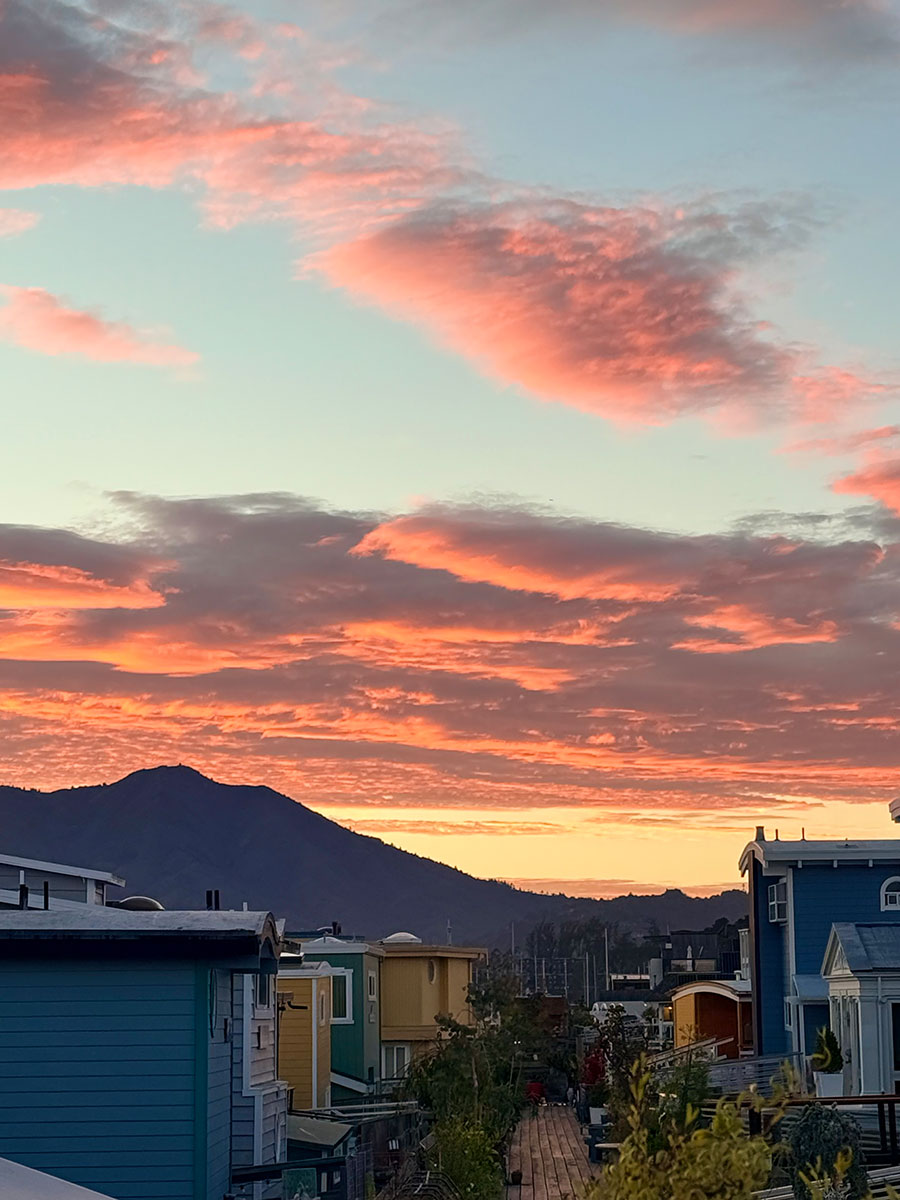 Sunset sky with vibrant pink and orange clouds over a mountain silhouette and houses.