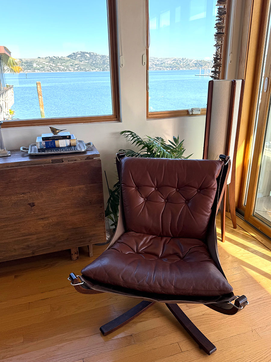Brown leather chair in a cozy room with wooden floors, large windows offering a tranquil lake view.
