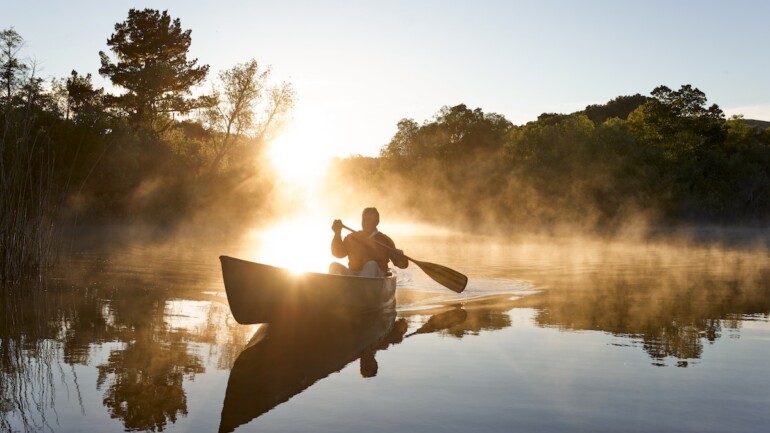 Person canoeing on a lake at sunrise