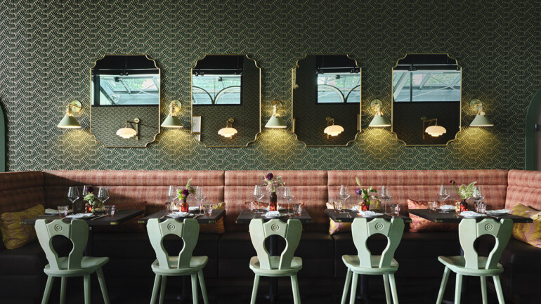 Elegant restaurant interior with patterned wallpaper, vintage mirrors, and wall sconces.