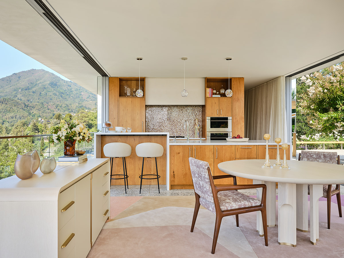 Modern kitchen with light wood cabinets, white countertops, and a scenic view of greenery through large windows