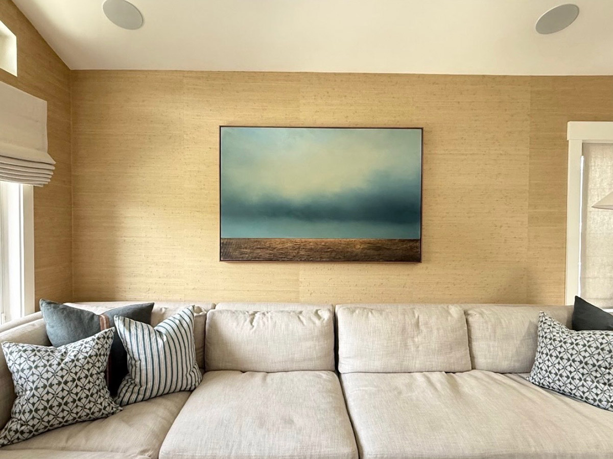 living room with a cream sectional sofa, patterned pillows, textured walls, and a moody ocean landscape painting above.
